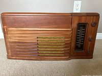 Front view of the wooden Philco radio console showing tuning dial and knobs, horizontal carved speaker slats, and wood grain.