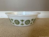 Side view of white Pyrex bowl showing green geometric floral pattern and handles.