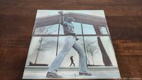 Front cover of Billy Joel Glass Houses vinyl album showing Billy Joel standing with fist raised in front of a glass building.