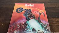 Front cover artwork showing motorcycle riding figure bursting out of graveyard and album title 'Bat Out Of Hell' by Meat Loaf