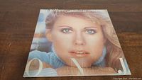 Front cover of Olivia Newton John Greatest Hits vinyl album showing close-up portrait photo of Olivia Newton John in a blue sweater.