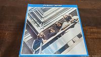 Front cover of The Beatles 1967-1970 vinyl album showing band members looking down from a balcony with a blue border and white text.