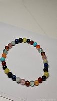 Single stretchy bracelet composed of round polished beads in multiple natural gemstone colors including yellow, blue, pink, amber, orange and others on a white background.
