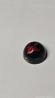 Close-up photo of a cabochon cut Ethiopian black opal showing bright flashes of red and green colors on a dark base.
