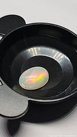 Oval cabochon cut Ethiopian fire opal in a black holder, showing characteristic fiery flashes of color.