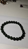Top view photo showing round dark green 8mm jade beads in a stretchy bracelet laid flat on white background.