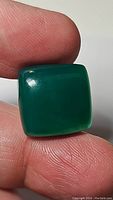 Square polished vivid green onyx gemstone held between fingers showing size and texture.