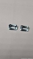 Pair of natural sky blue topaz gemstones in emerald cut, matching size and color, placed on neutral background