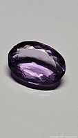 Close-up photo of the 9.86ct oval cut Brazilian amethyst, showing the deep purple faceted gemstone with very high clarity and reflective surface.