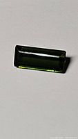 Rectangular bright green natural tourmaline gemstone placed on a light background showing the color and cut details.