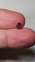 Close-up image of a bright deep pink pear teardrop rhodolite garnet gemstone held between fingers, showing clarity and color.