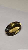 Oval cut champagne citrine gemstone on plain background showing facets and color.