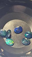 Close-up photo of five oval cut Ethiopian black opal gemstones showing multicolored flashes inside a black container.