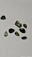 Photo showing 9 individual green tourmaline gemstones in various shapes and sizes on a white background.
