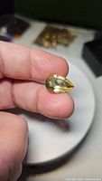 Pear-shaped lemon citrine gemstone held between fingers, showing clarity and color.