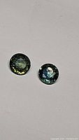 Pair of round faceted multicolored sapphires on a plain background showing color and clarity.