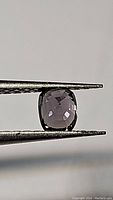 Cushion cut purple spinel held in tweezers showing top view with facets and clarity in natural light.