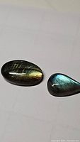 Two polished natural labradorite cabochons with distinct flashes of color, one oval and one pear shaped.