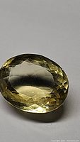 Oval cut natural lemon citrine gemstone with faceted surface and lemon yellow color on a white background.