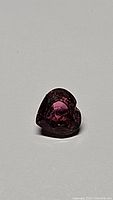 Heart-shaped deep red purple Rubelite tourmaline gemstone photographed from a front angle on a plain background.