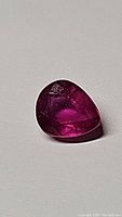 Pear shaped ruby gemstone with vivid red pink color on light surface, showing internal inclusions and reflective highlights