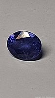 Close-up photo of the oval cut natural tanzanite gemstone on a plain background showing its deep blue color and faceted surface.