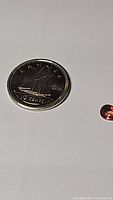 Photo of a 2018 Canadian 10 cent coin placed next to a small pear-shaped padparadscha sapphire. Used for size scale comparison.