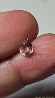 Pear-shaped padparadcha tourmaline gemstone showing its pink to orange tones, held between fingers for size reference.