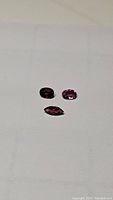 Three pink purple garnet gemstones on white background, showing different shapes and clarity.