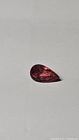 Photo of single pear-shaped pink tourmaline gemstone on plain background showing color and cut.