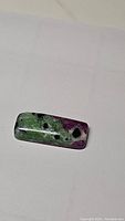 Polished rectangular ruby zoisite cabochon showing natural green zoisite matrix and ruby inclusions.