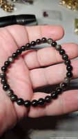 Photo of stretchy bracelet held in hand, showing reflective silver sheen obsidian polished round beads.
