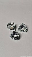 Close-up photo of three natural untreated aquamarine gemstones with trillion cut, showing their color and clarity.