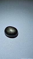 Oval cabochon untreated black star sapphire on a light background with light reflecting to show star effect.