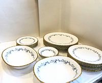 Photo showing all plates and bowls stacked and arranged with clear view of blue floral and gold scalloped trim decoration on white bone china.