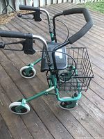 Side view of green metal assistive walker showing black foam handle grips, lever brakes and basket.