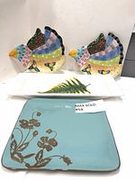 Pair of colorful ceramic bird-shaped trays, white fern leaf rectangular tray, blue Fitz & Floyd floral plate, and blue Gibson Elite plate arranged together