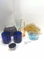 Full lot view showing multiple glass items including two blue cylindrical vases, a purple basket, peach basket, golden brown centerpiece, teal glass, salt cellar, and small blue item.
