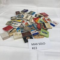 Photo showing a large grouping of vintage matchbooks spread on a white surface, diverse in color and design.