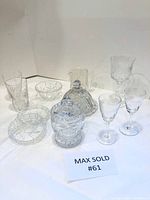 Top-down image showing the entire lot of 11 clear glass pieces on white background including glasses, small bowls, and covered jars.