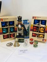 Photo showing Woolworth boxed vintage Christmas ball ornaments in blue, green, red, and gold colors alongside a wooden musical nutcracker and several small Christmas-themed figurines including a polar bear, Santa, angel, and elf.