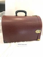 Side view of the closed hard-sided pet carrier showing red and black checkered pattern and brass latch on one side.