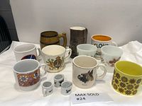 Lot showing all 11 vintage coffee mugs arranged on white fabric, some with visible chips and varying designs.