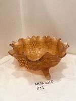 Marigold carnival glass footed bowl showing ruffled edge, grape and leaf pattern and three claw feet from an angle