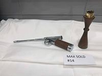 Two vintage lighters placed on white cloth, one is a gun-shaped lighter with chrome and wood finish, the other is an hourglass wooden lighter with a brass top.