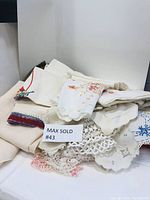 Various folded vintage linens including embroidered tablecloths, doilies, and runners with lace and crochet details.