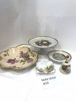 Lot including porcelain cake stand, trinket dish, decorative bell, and plates shown together on white background