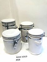Four white ceramic canisters with metal latching lids, arranged on surface showing their black rim accents and locking mechanisms.