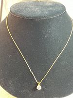 Full view of the fine delicate 10 karat gold chain necklace with small clear stone pendant displayed on a black velvet bust.