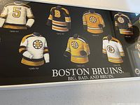 Close-up photo of printed illustration showing six vintage Boston Bruins jerseys dated 1920-21, 1937-74, 1941-57, 1948-49, 1962-65, and 1971-74.
